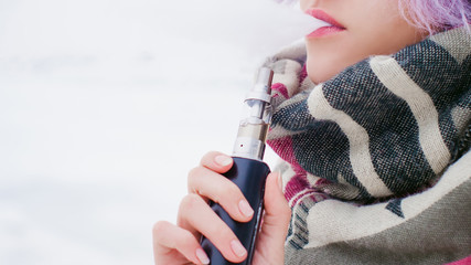 vaping girl. winter street portrait of a woman hipster, purple-dyed hair, a gray knitted hat and...
