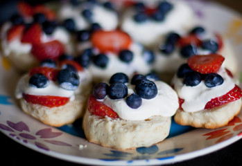 Scones with blueberries, strawberries and clotted cream on plate.
