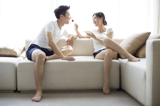Happy young couple eating fruit salad on sofa