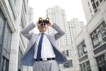 Confident businessman looking through binoculars