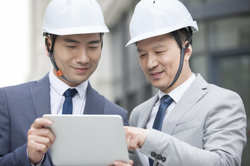 Male architects talking with digital tablet outdoors