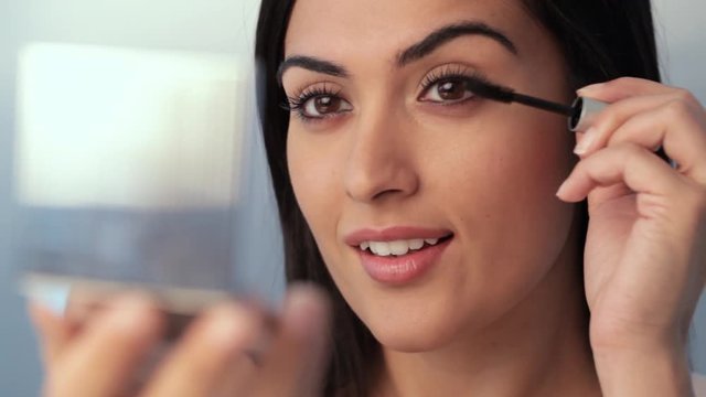 CU SELECTIVE FOCUS Young woman applying mascara to eyelashes, studio shot