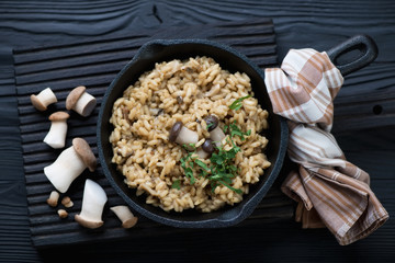 Frying pan with porcini risotto over black wooden background