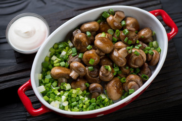 Closeup of roasted champignons served with green onion in a bowl