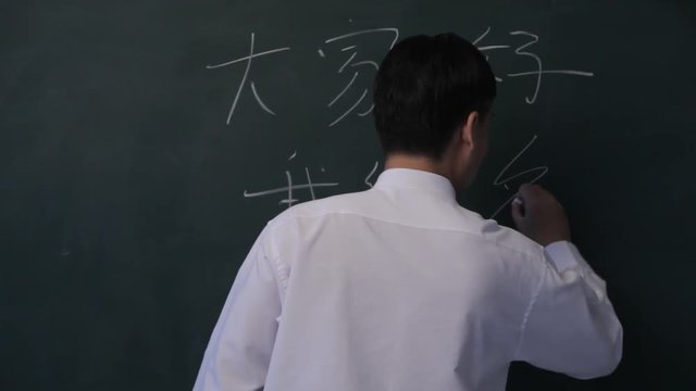 MS PAN Man writing Chinese characters on blackboard, turning to look at camera