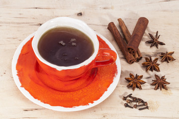 Cup of tea with anise stars , cinnamon sticks and cloves on wooden plank