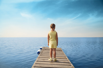 Fototapeta na wymiar Little girl standing at wooden pier and looking to the sea