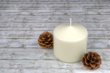 Fototapeta na wymiar Weiße Kerze mit Tannenzapfen auf hellem Holz