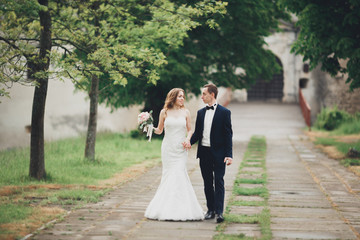 Beautiful couple of happy stylish newlyweds walking in the park on their wedding day with bouquet