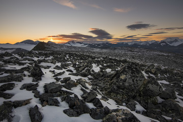 Fototapeta na wymiar Stone field covered with snow on Laddebakte top, with beautiful orange sunset background