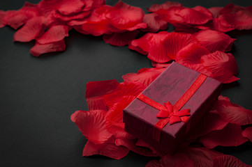 Valentine’s day concept with a valentine gift box on red rose petals against a black background with copy space
