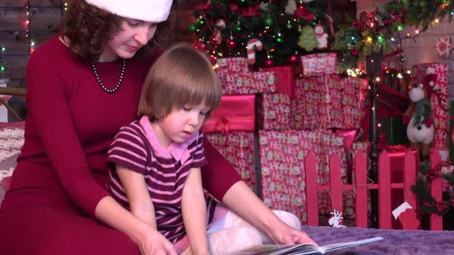 Mom shows daughter pictures in a book, xmas decorations