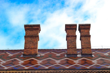 Three chimney from red brick on the old roof of colored tiles