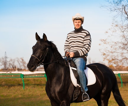 Man riding horse, striped pullover, blue jeans, hat, close up