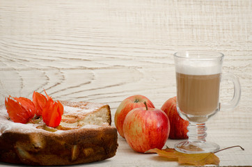 Homemade apple pie, cappuccino and ripe apples on a light wooden background