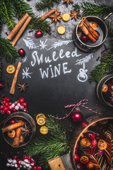 Traditional mulled wine  ingredients with cooking pot ,mugs and fir branches on black chalkboard background, top view, frame