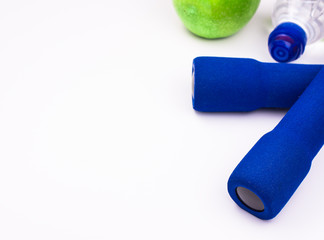 Blue dumbbells with a bottle of water and a green apple on a white gym floor, copyspace for text