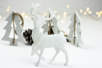 White Christmas decoration in scandinavian style with reindeer, wood fir treeas and pine cones, bokeh lights in the background