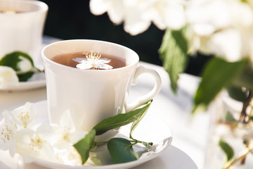 Obraz na płótnie Canvas Close up on jasmine tea with jasmine flower in a glass cup. Tea service in the garden.