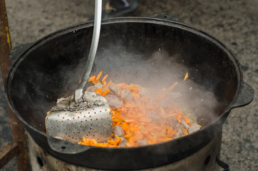 Cooking meat outdoors in cast-iron cauldron.