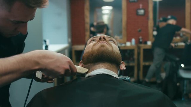 Young hipster Caucasian man during beard and mustache grooming in modern barber shop. 4K UHD RAW edited footage