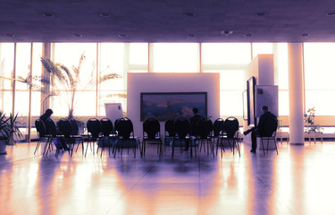 Few people sitting on chairs in modern auditorium waiting for seminar to begin