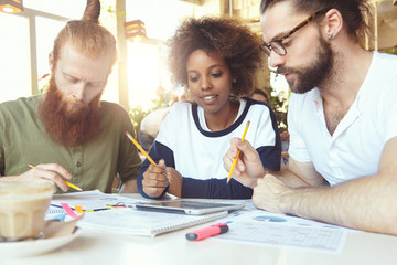 Brainstorming concept. Crew of experts sitting at table with papers and digital tablet, discussing business strategy, plans and ideas of their collaborative project, making notes using pencils