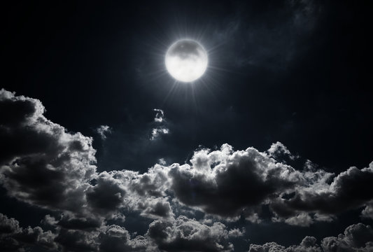 Dramatic photo illustration of a nighttime sky with brightly lit clouds and large. Beautiful starry night sky with clouds and bright full moon or super moon.