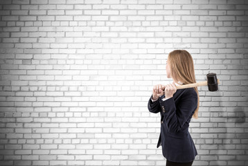 Woman crashing white brick wall with sledgehammer