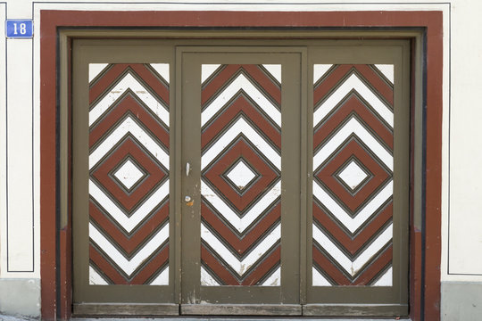 A wooden garage door with diamond pattern painted in brown, white and red color