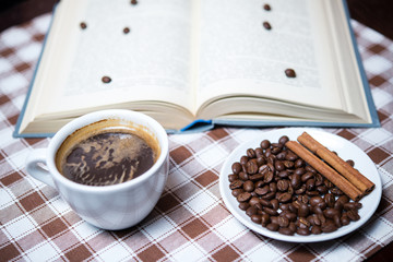 cup of coffee with beans and book on the tablecloth closeup