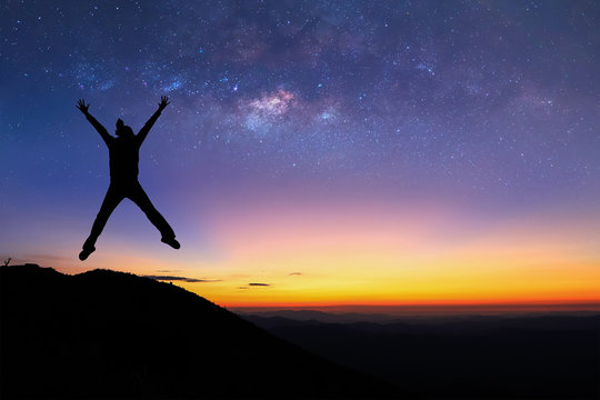 Silhouette of woman is jumping on top of mountain and enjoy to see the milky way before sunrise.
