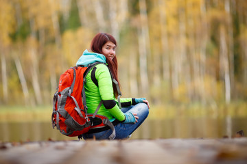 Brunette with backpack sitting on bridge at lake