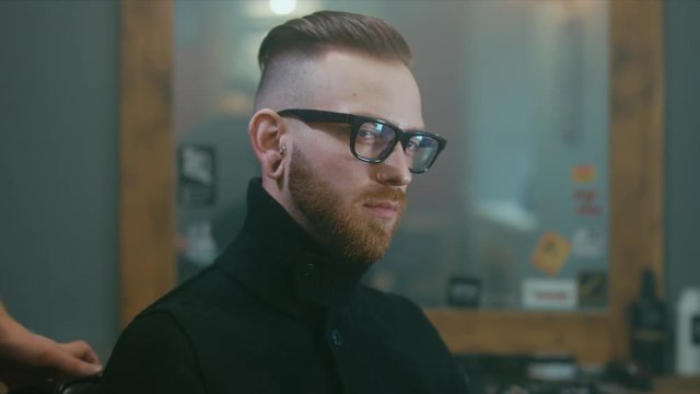 Young satisfied Caucasian man drinking whiskey after a getting haircut in a modern barber shop. 4K UHD Raw edited footage