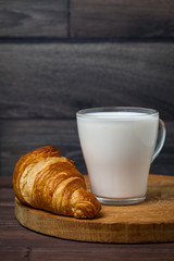 Croissant and a transparent glass of milk. On a wooden table. Healthy diet.