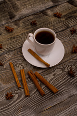 Small white cup of coffee, cinnamon sticks, star anise on wooden background