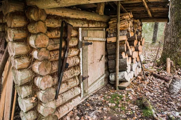 Foto auf Leinwand Hunting lodge in the forest. At the entrance hangs a hunting rifle. Cloudy weather on earth is some snow. Near the wooden house stacked firewoods. © scharfsinn86