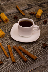 Small white cup of coffee, cinnamon sticks, star anise and cookies on wooden background