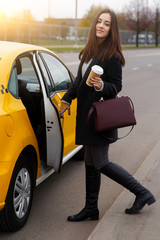 Beautiful brunette in black coat opening door of yellow taxi