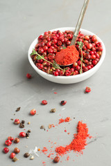 pink peppercorns and ground pepper on a gray background