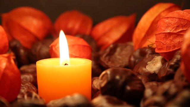 Kerze brennt zwischen Lampionblumen und Kastanien