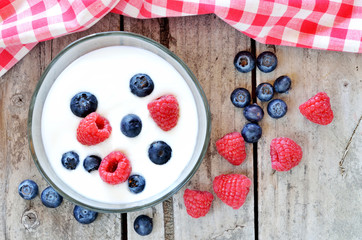 White yogurt in a bowl with blueberries and raspberries on wooden table