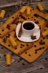 Small white cup of coffee, cinnamon sticks, cocoa beans, star anise and cookies on wooden background