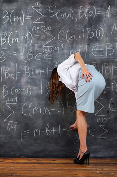 sexy young teacher writing on large blackboard maths formulas