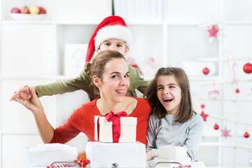 Two kids and their mother are opening Christmas pressents in their lliving room. They are having a lot of fun.