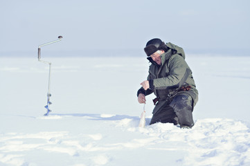 Fototapeta na wymiar A fisherman in the winter fishing rod in the hole near the drill.