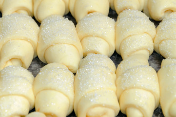 Raw croissants on metallic oven-tray closeup.