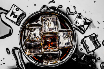 Glass with cola and ice cubes surrounded by ice cubes and water drops
