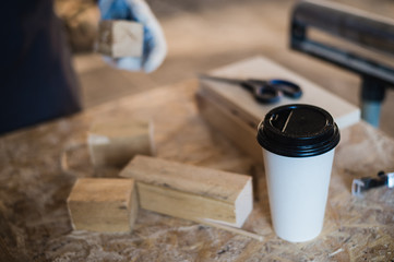 Modern carpentry work place with tablet, coffee, scissors and wooden pieces on table, in workshop