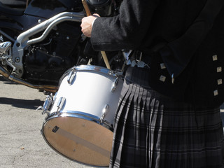 Man with kilt playing on drums . Closeup of motorcycle for background
